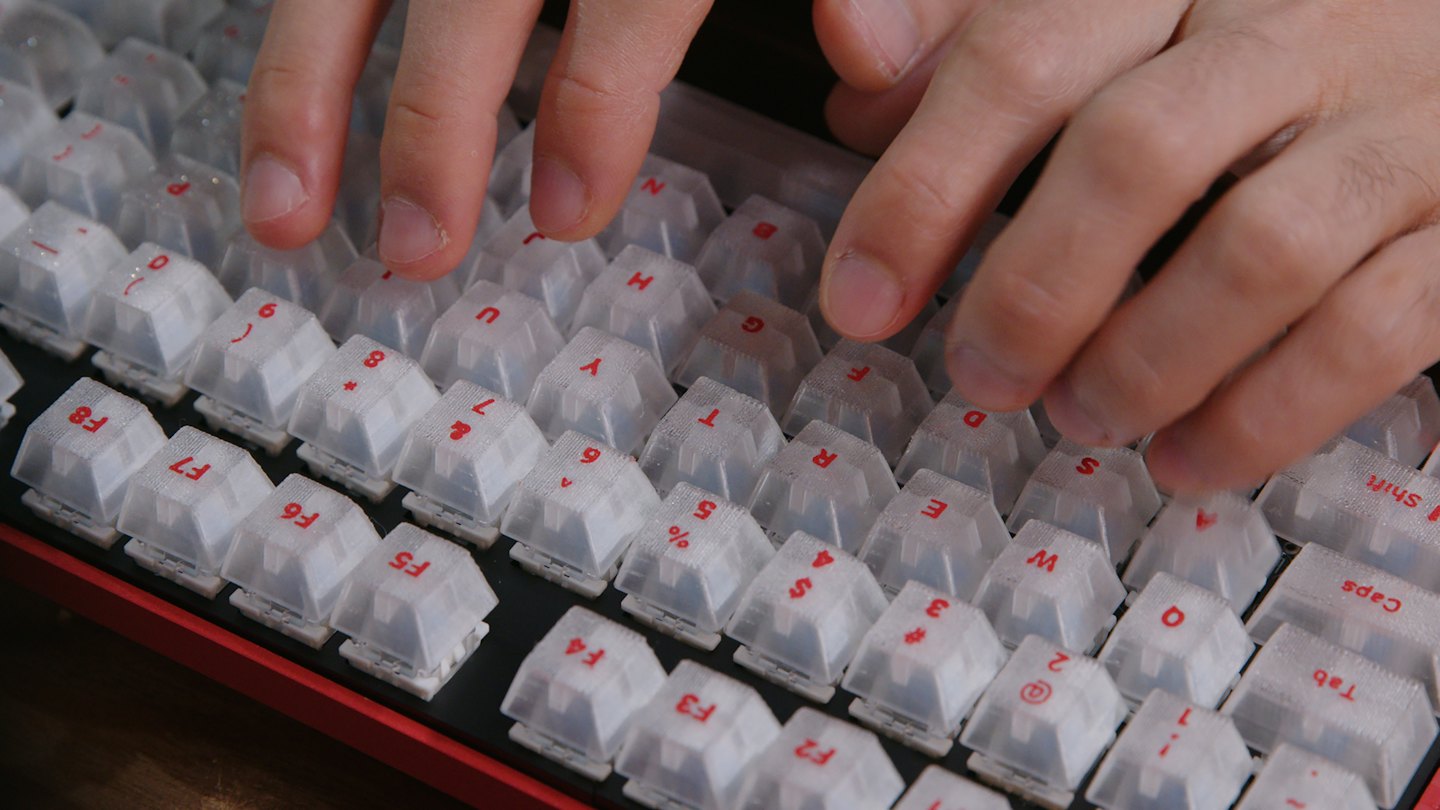 Manos escribiendo en un teclado mecánico rojo y negro con teclas blancas.